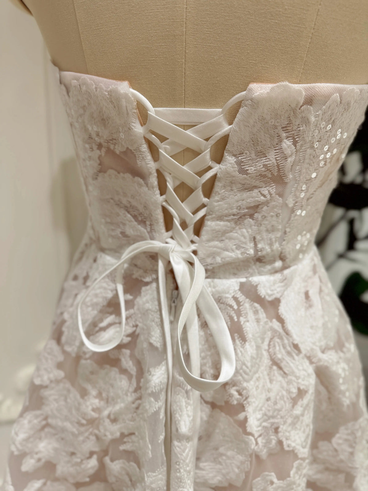 White strapless bridal mini dress featuring floral embroidered lace, shimmering sequins, and an adjustable lace-up corset back.