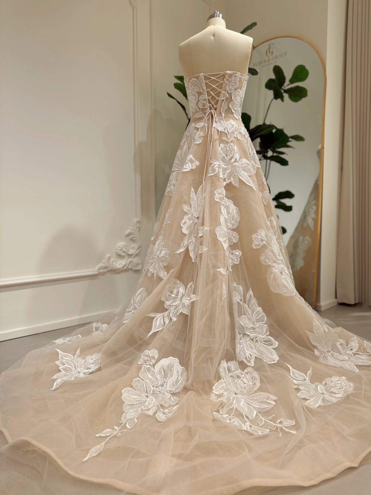 Strapless nude tulle wedding gown with white floral embroidery, rhinestone accents, lace-up back, and chapel train.