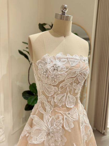 Strapless nude tulle wedding gown with ivory floral embroidery, rhinestone embellishments, and a structured corset bodice.