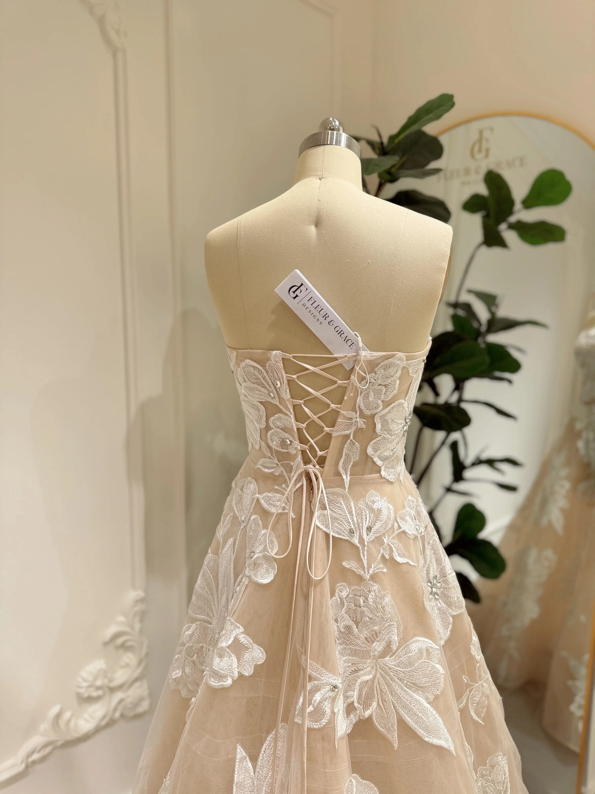 Strapless Mira wedding gown in nude tulle with white floral embroidery, rhinestone accents, and lace-up corset back.