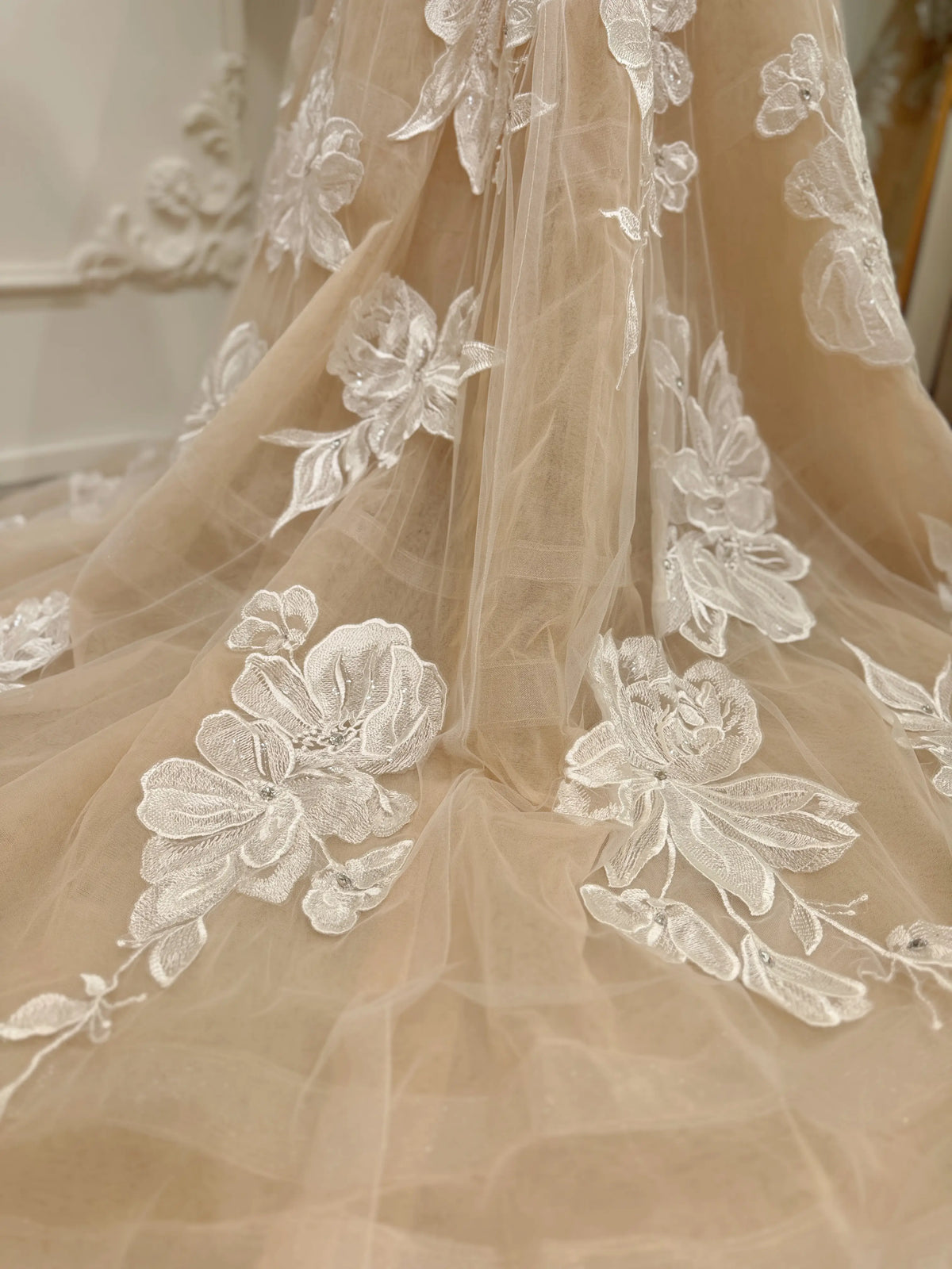Nude tulle wedding dress with ivory floral embroidery and delicate rhinestone embellishments on a chapel train.