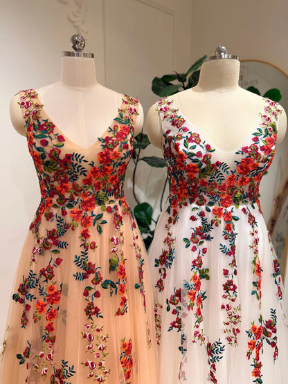 Two Monica A-line wedding dresses featuring vibrant floral embroidery on layered tulle in champagne and ivory.