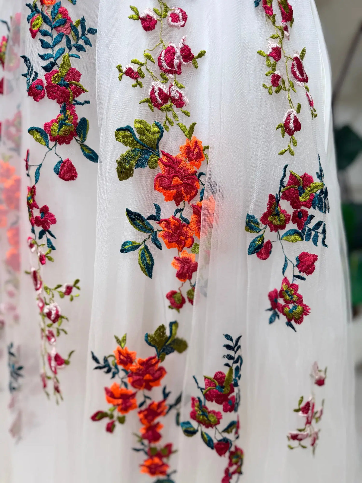 Close-up of white tulle wedding dress featuring vibrant floral embroidery in pink, orange, and green garden tones.