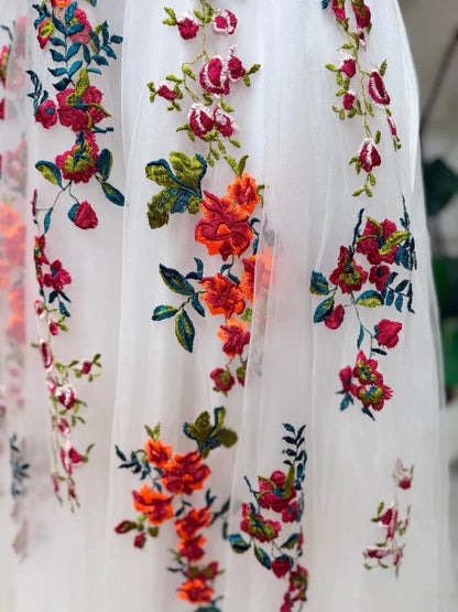 Close-up of white tulle wedding dress featuring vibrant floral embroidery in pink, orange, and green garden tones.