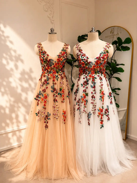 Two Monica A-line wedding dresses in champagne and white with vibrant floral embroidery on layered tulle.