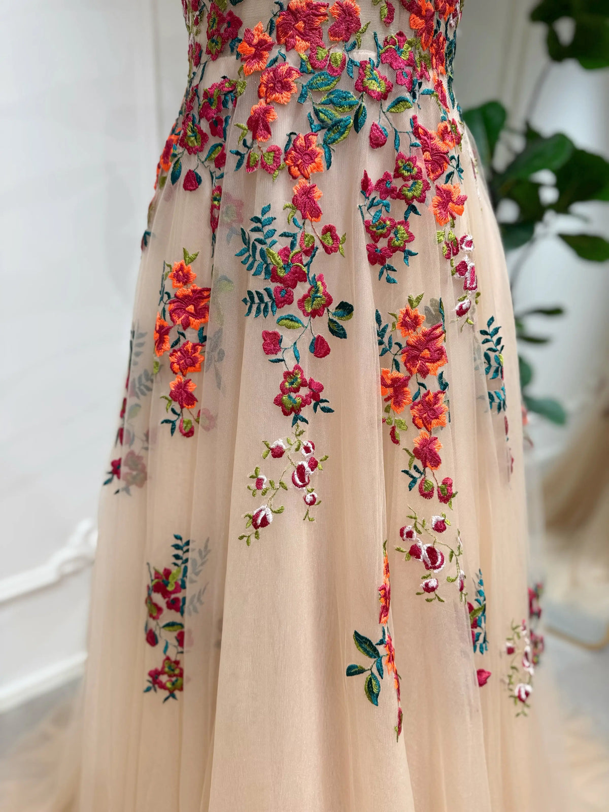 Champagne tulle wedding dress featuring vibrant orange and pink floral embroidery with green meadow foliage.