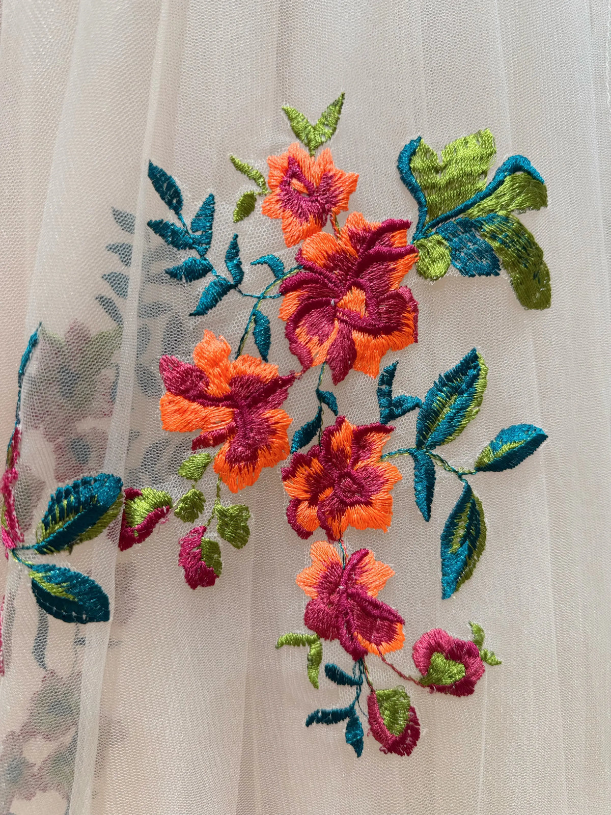 Vibrant orange and magenta floral embroidery with green leaves on sheer champagne tulle bridal fabric.
