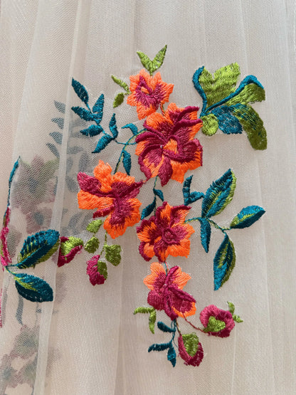 Vibrant orange and magenta floral embroidery with green leaves on sheer champagne tulle bridal fabric.