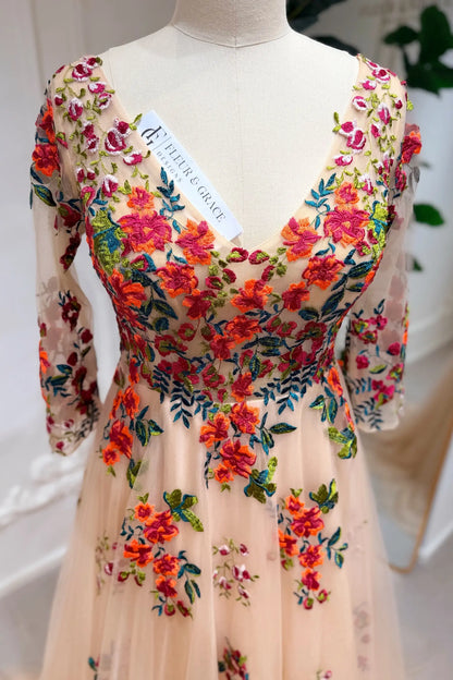 Champagne tulle wedding gown with vibrant orange floral embroidery, V-neckline, and 3/4 lace sleeves on a mannequin.