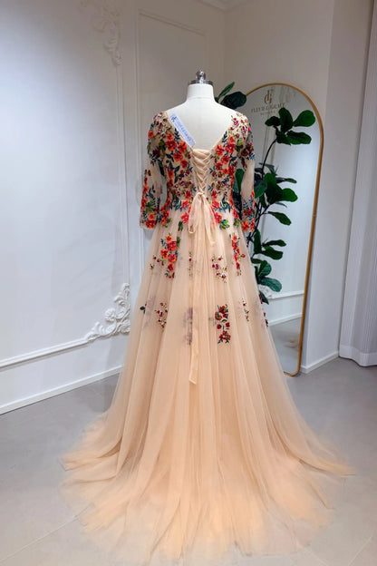 Monica Gown by Fleur&Grace Designs — champagne tulle A-line wedding dress with orange and red floral embroidery, meadow green vines, V-neckline, 3/4 lace sleeves, lace-up back, and pockets for whimsical brides.