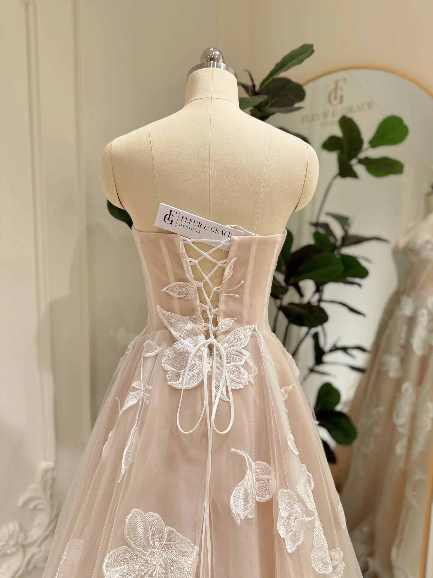 Strapless nude tulle wedding dress with ivory floral appliqués and a lace-up corset back on a mannequin.