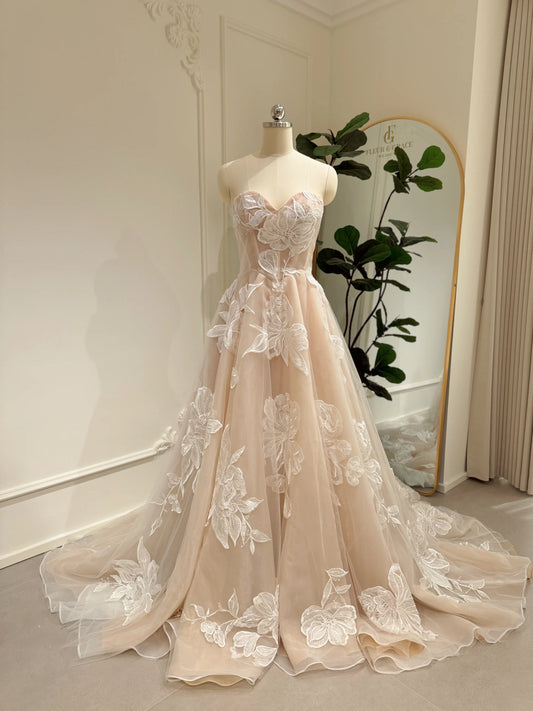 Strapless nude tulle wedding dress with ivory floral appliqués, sweetheart neckline, basque waist, and cathedral train.