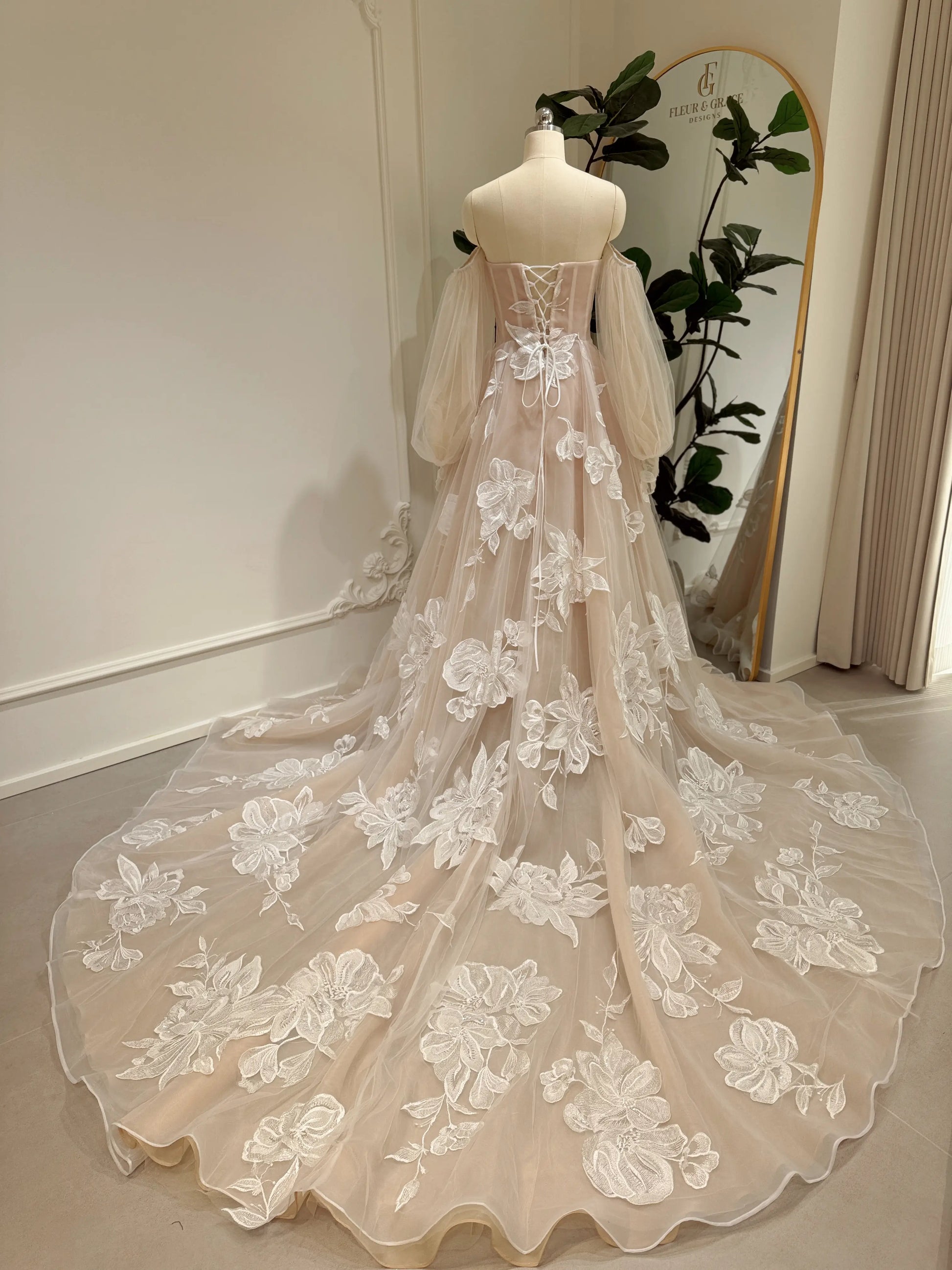 Nude tulle wedding dress with ivory floral appliqués, puff sleeves, basque waist, lace-up back, and cathedral train.