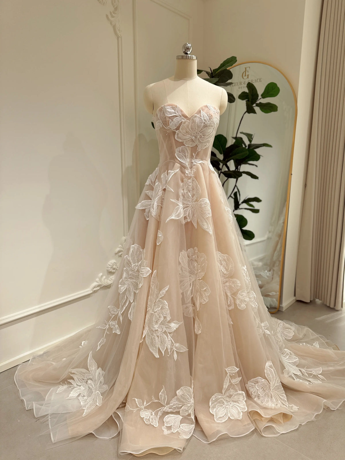 Strapless nude tulle wedding dress with ivory floral appliqués, sweetheart neckline, and a flowing cathedral train.