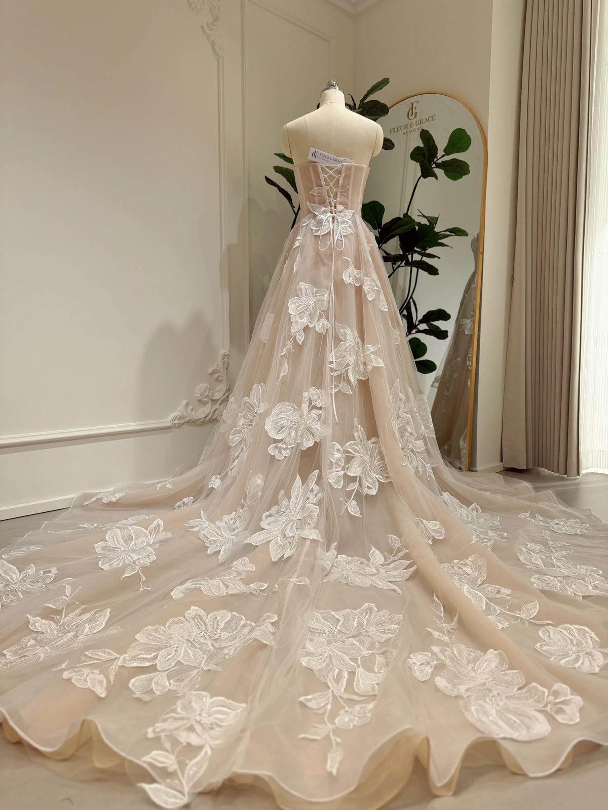Nude tulle wedding dress with ivory floral appliqué, basque waistline, lace-up back, and a dramatic cathedral train.