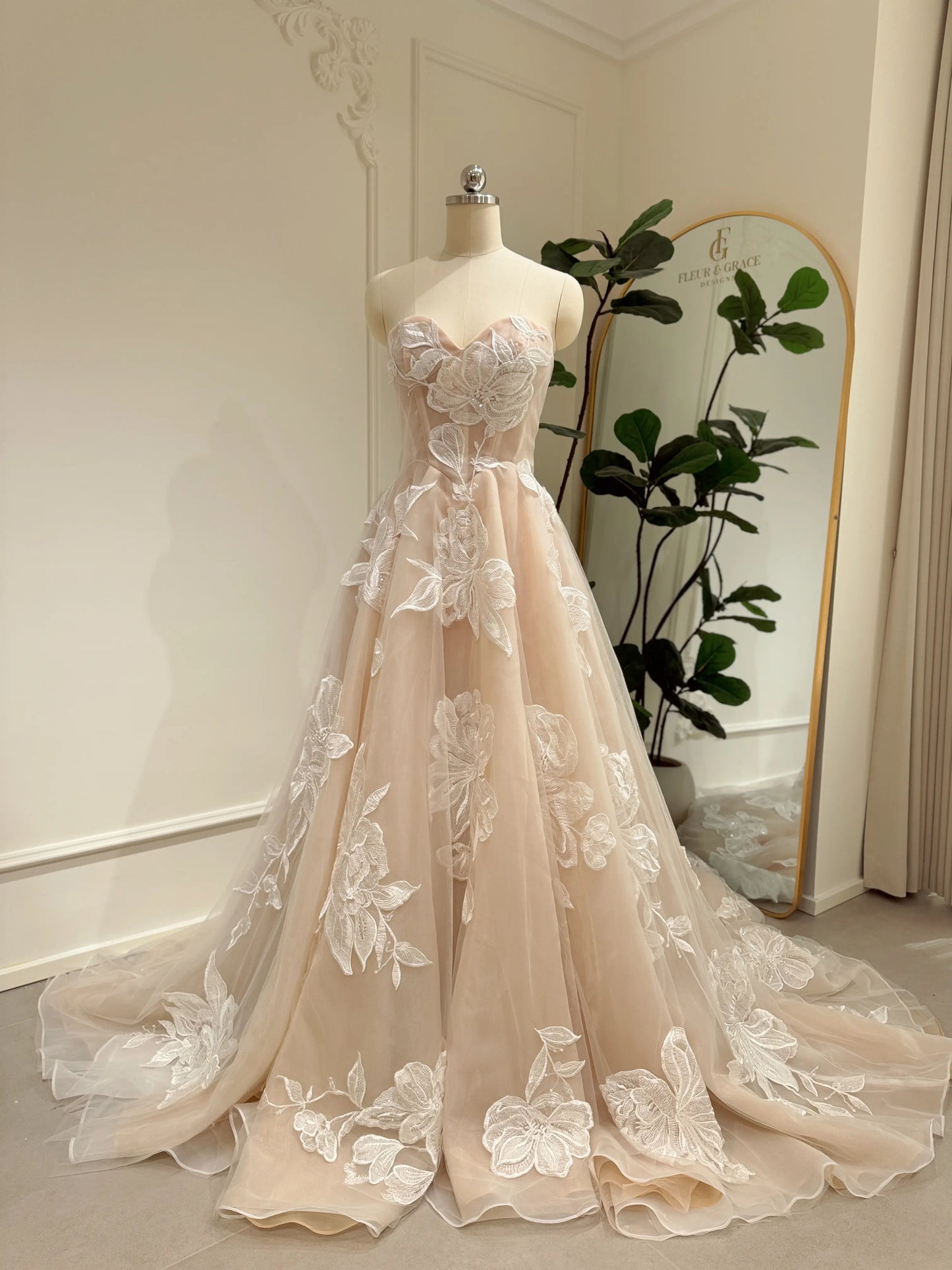 Strapless nude tulle wedding dress with ivory floral appliqués, sweetheart neckline, and a dramatic cathedral train.