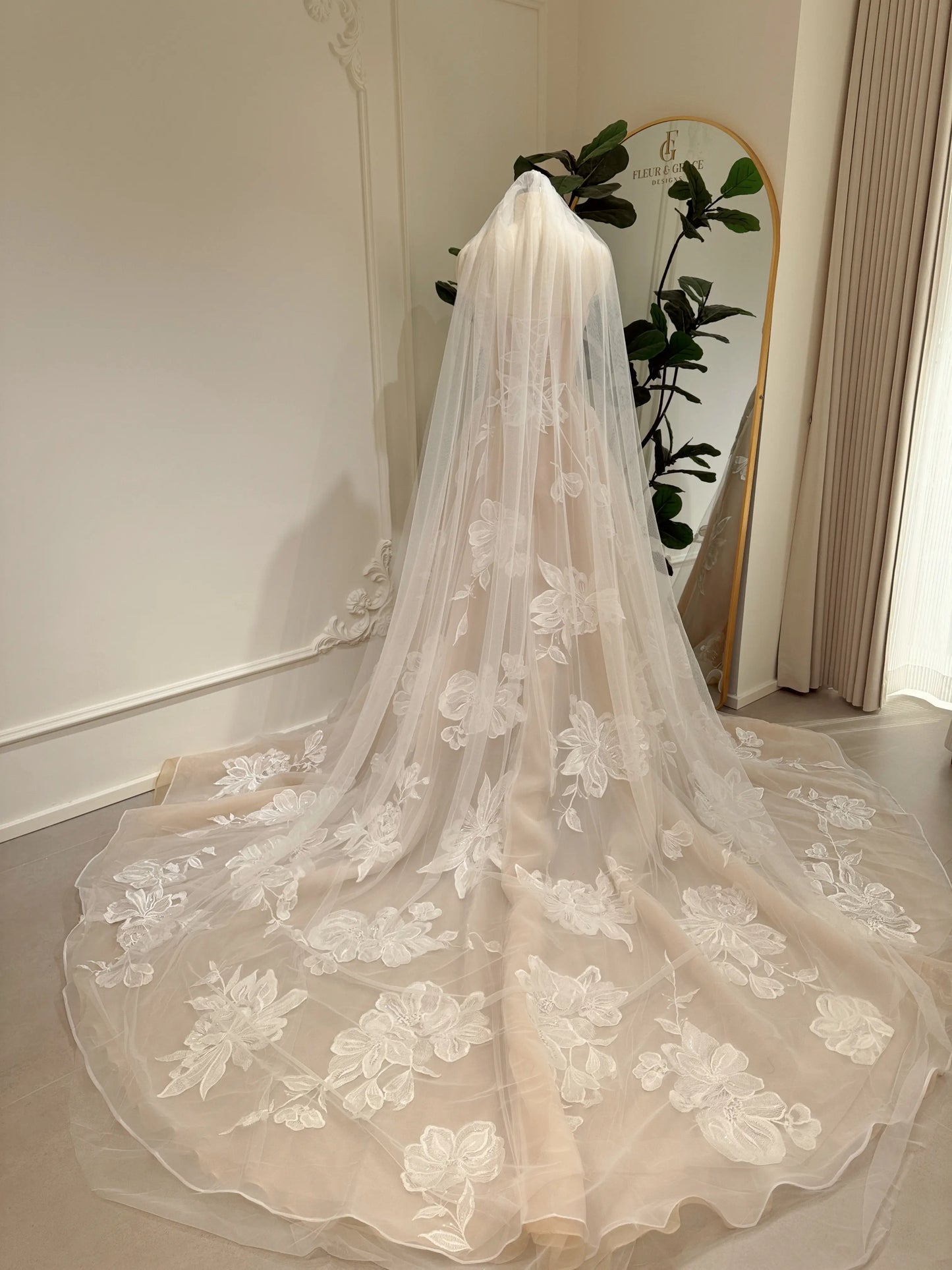 Nude tulle wedding dress with ivory floral appliqué and a dramatic cathedral-length train on a mannequin.