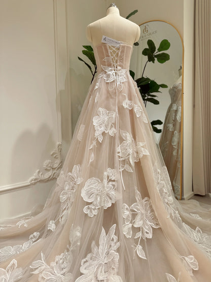 Nude tulle wedding dress with ivory floral appliqués, basque waistline, and lace-up back on a mannequin.