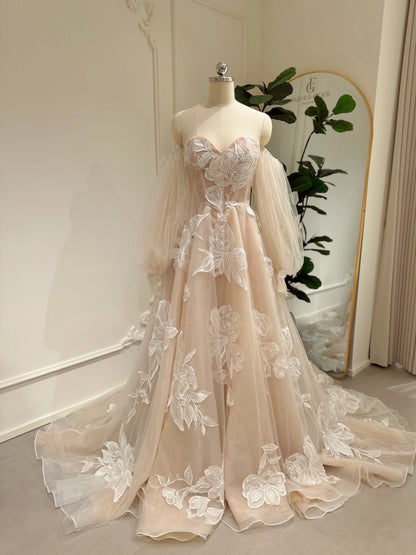 Nude tulle wedding dress with ivory floral appliqués, sweetheart neckline, basque waist, and removable puff sleeves.