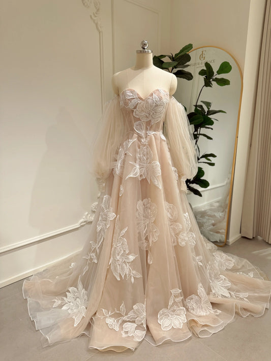 Nude tulle wedding dress with ivory floral appliqués, sweetheart neckline, basque waist, and removable puff sleeves.