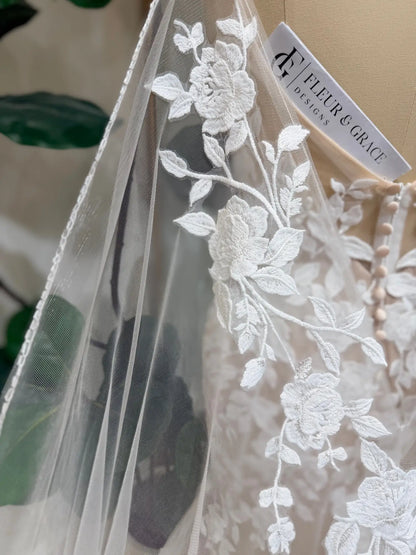 Close-up of Nola mermaid wedding dress featuring delicate white floral lace appliqué over soft nude tulle lining.