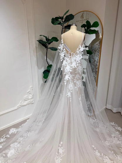Nola mermaid wedding dress with floral lace appliqué, nude lining, and a dramatic, flowing detachable tulle cape.