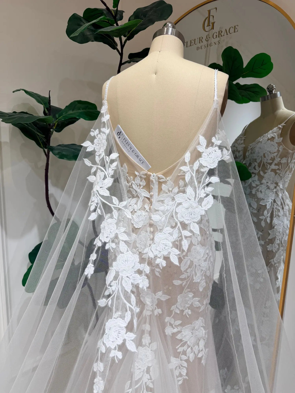 Nola mermaid wedding dress with floral lace appliqué, nude illusion lining, and a dramatic detachable tulle cape.
