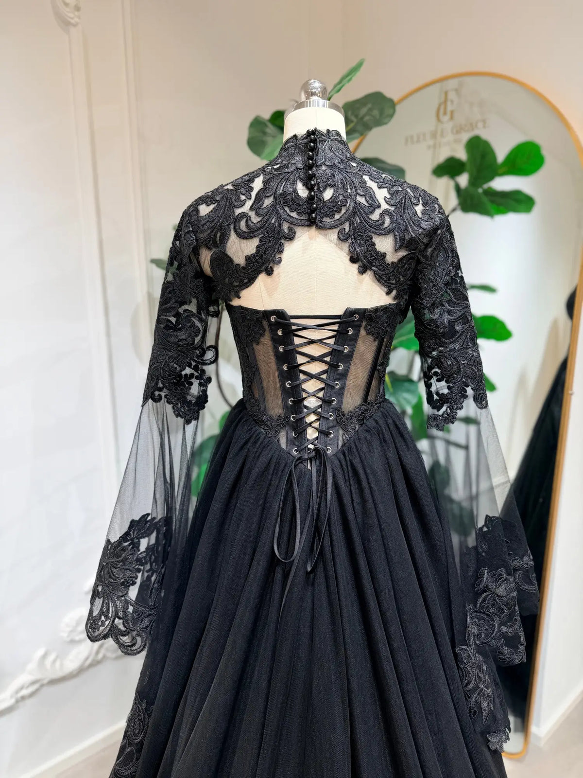 Black gothic wedding dress with intricate lace, sheer detachable sleeves, and a corset back on a mannequin.