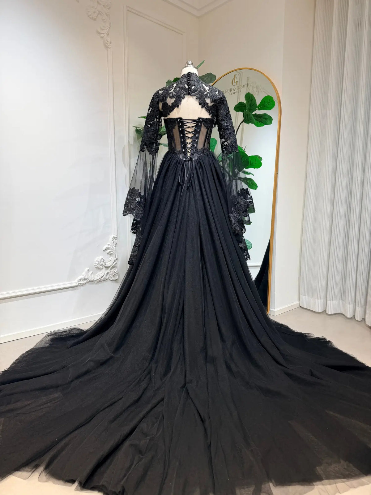 Black gothic wedding dress with lace-up corset back, intricate floral lace, and dramatic tulle train with sheer sleeves.