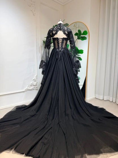 Black gothic wedding dress with lace-up corset back, intricate floral lace, and dramatic tulle train with sheer sleeves.
