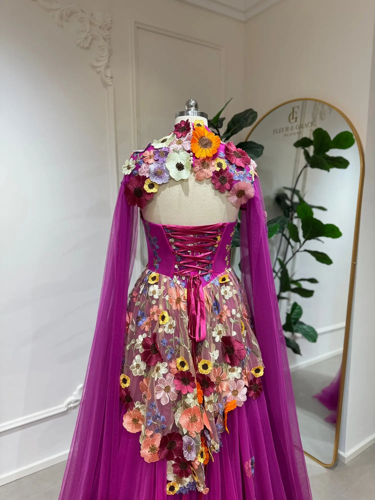 Magenta floral appliqué corset gown with lace-up back, detachable cape sleeves, and a voluminous tulle skirt.