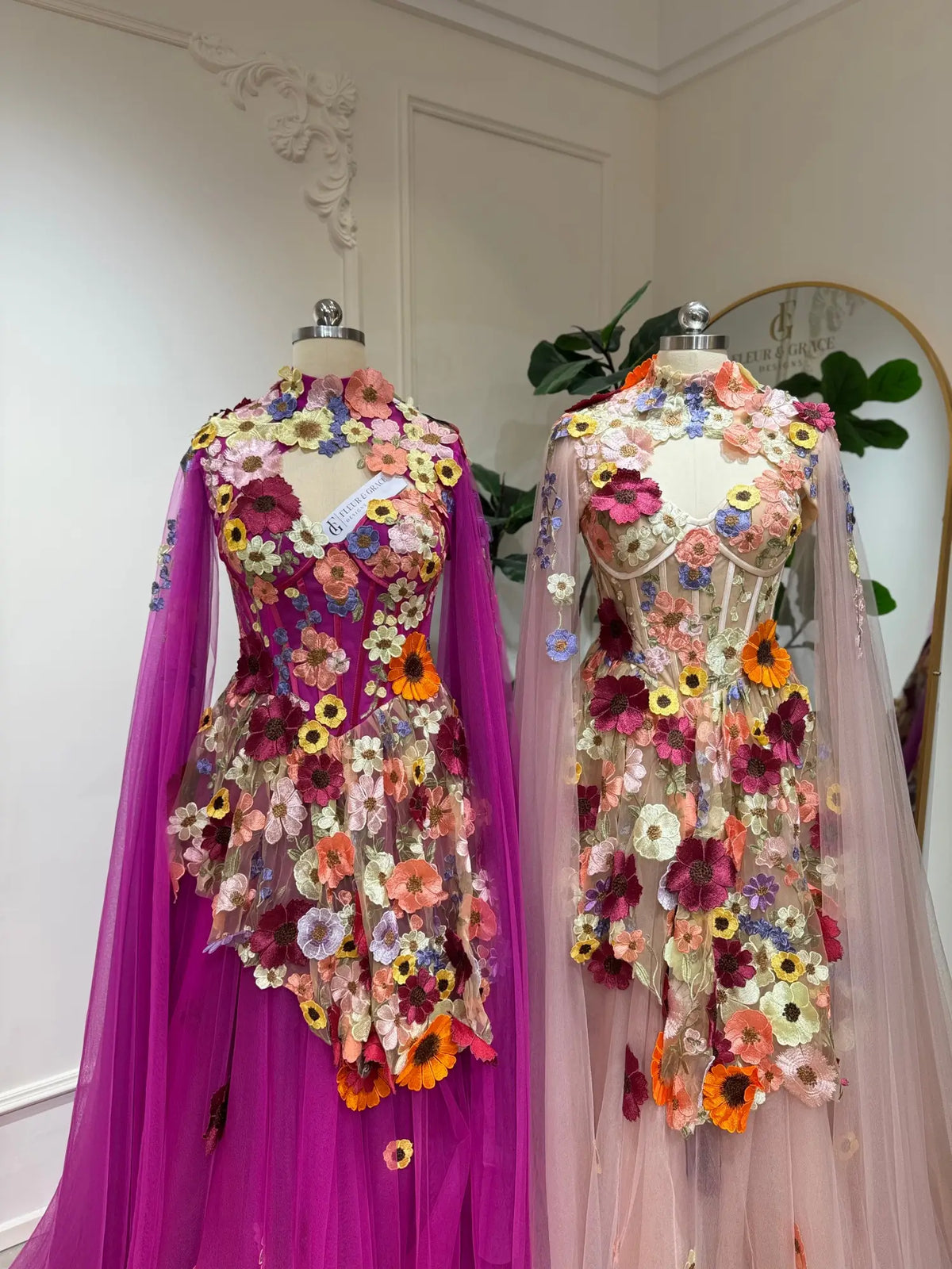 Magenta and blush tulle corset gowns featuring 3D floral appliqués and elegant detachable cape sleeves.