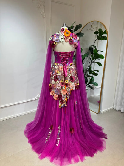 Magenta tulle corset gown with 3D floral appliqués, lace-up back, and detachable sheer cape sleeves.