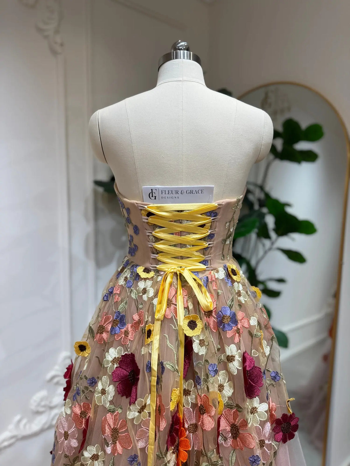 Blush pink tulle ball gown featuring a lace-up corset back and vibrant 3D floral appliqué embroidery.