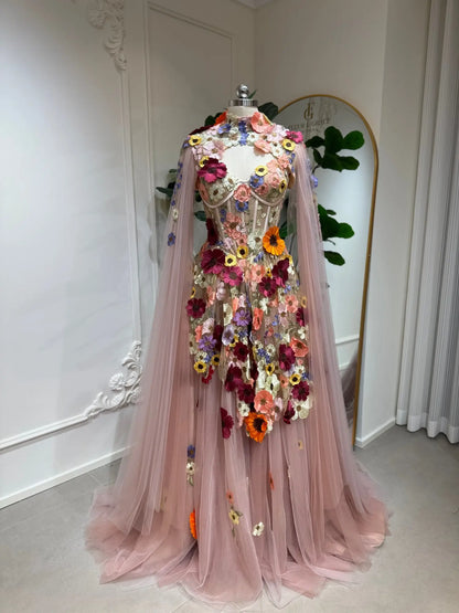 Blush pink tulle ball gown with 3D floral appliqués, corset bodice, and detachable sheer cape sleeves.
