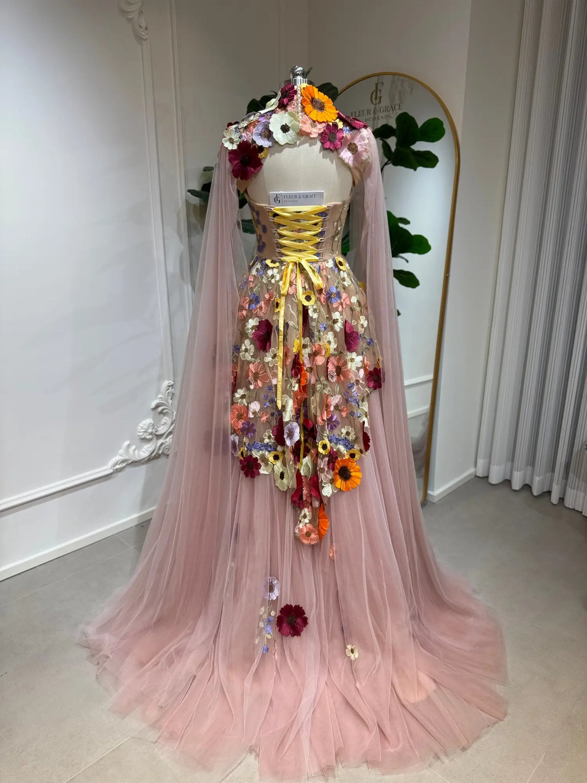 Blush pink tulle ball gown with 3D floral appliqués, corset lace-up back, and detachable sheer cape sleeves.