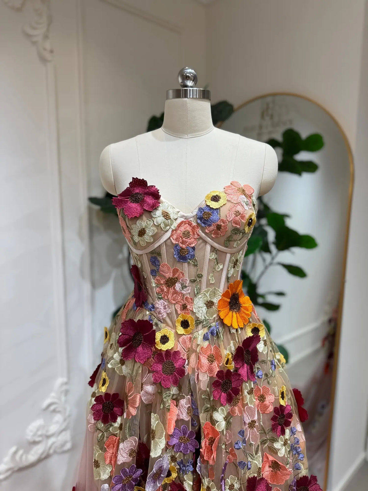 Blush pink corset ball gown featuring 3D multicolor floral appliqués and a structured, boned bodice on a mannequin.