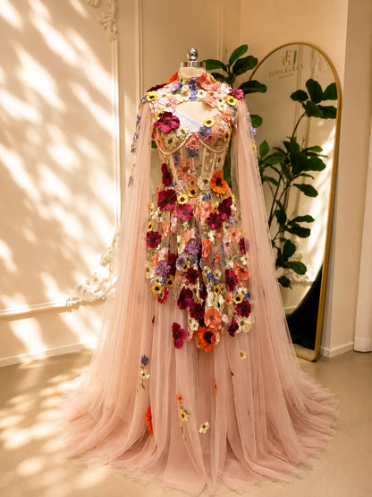 Blush pink tulle ball gown with 3D floral appliqués, a structured corset bodice, and elegant detachable cape sleeves.