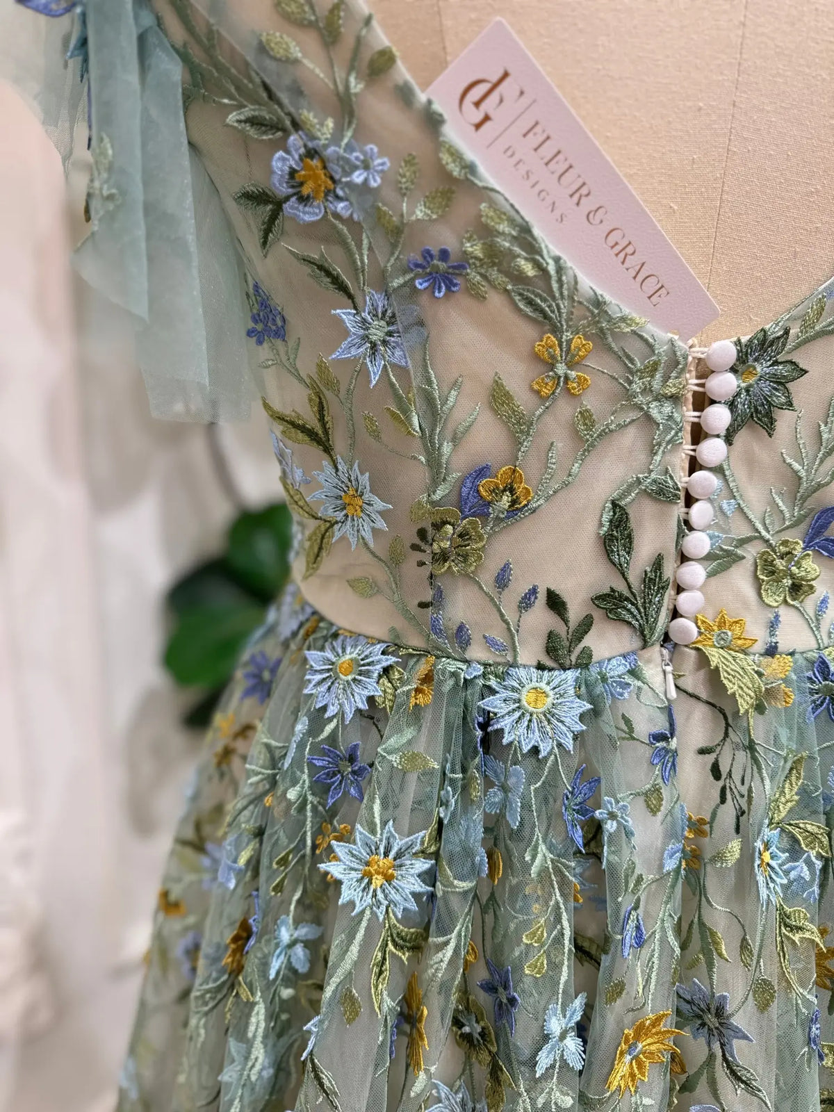 Sage green tulle gown with blue and yellow floral embroidery, corset bodice, and delicate sheer angel sleeves.