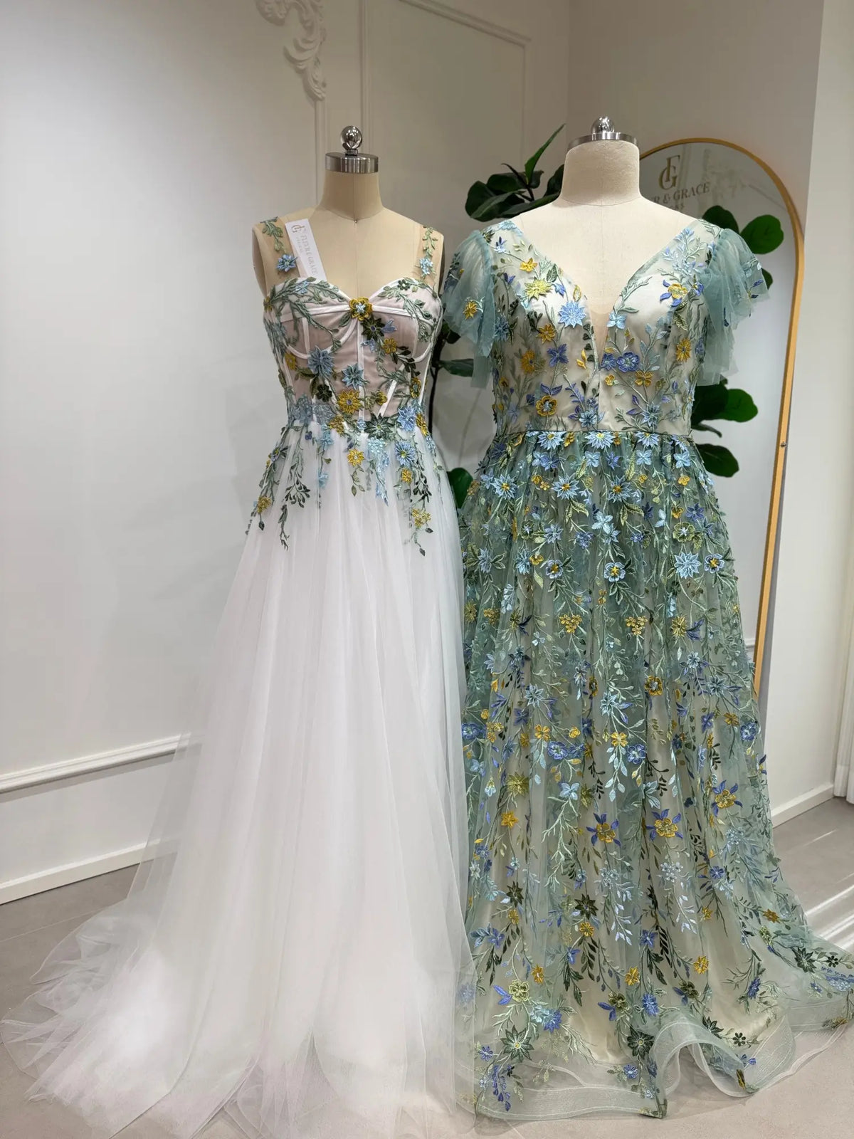Sage green and white tulle gowns featuring delicate blue, ivory, and yellow floral embroidery with angel sleeves.