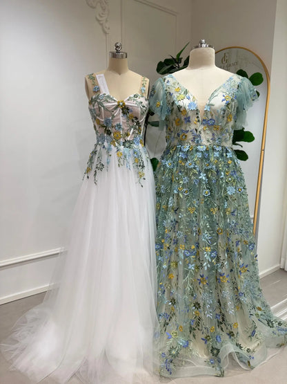 Sage green and white tulle gowns featuring delicate blue, ivory, and yellow floral embroidery with angel sleeves.
