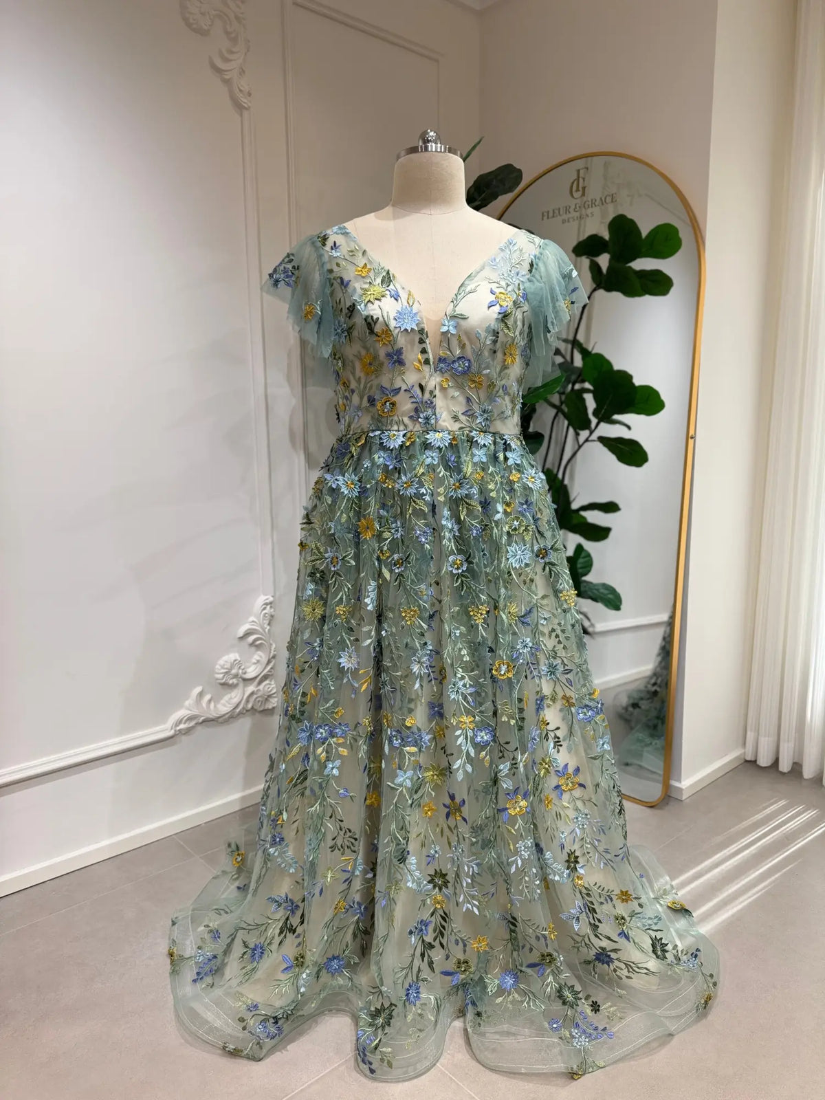 Sage green tulle gown with blue and yellow floral embroidery, corset bodice, and whimsical angel sleeves.