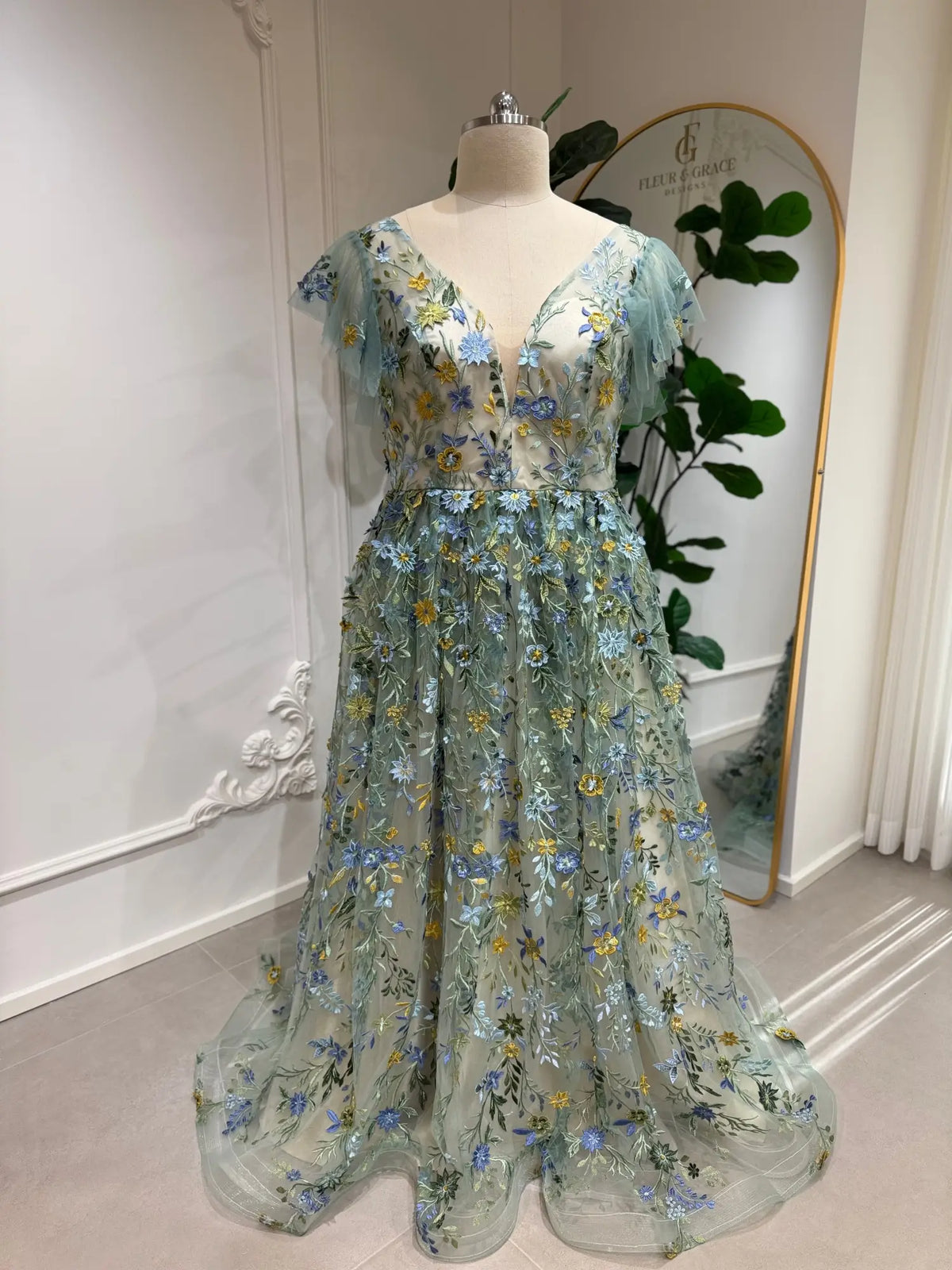 Sage green tulle gown with blue and yellow floral embroidery, corset bodice, and whimsical angel sleeves.