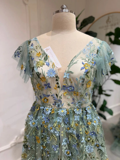 Sage green tulle gown featuring delicate blue and yellow floral embroidery, corset bodice, and whimsical angel sleeves.