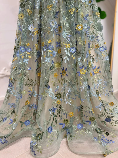 Sage green tulle gown featuring delicate blue, ivory, and golden yellow floral embroidery in a flowing A-line silhouette.