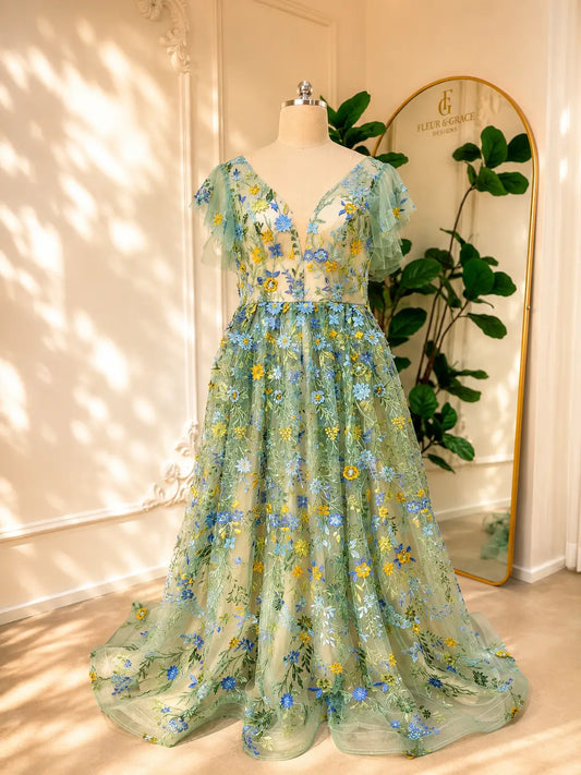 Sage green tulle gown featuring delicate blue and yellow floral embroidery, a corset bodice, and whimsical angel sleeves.