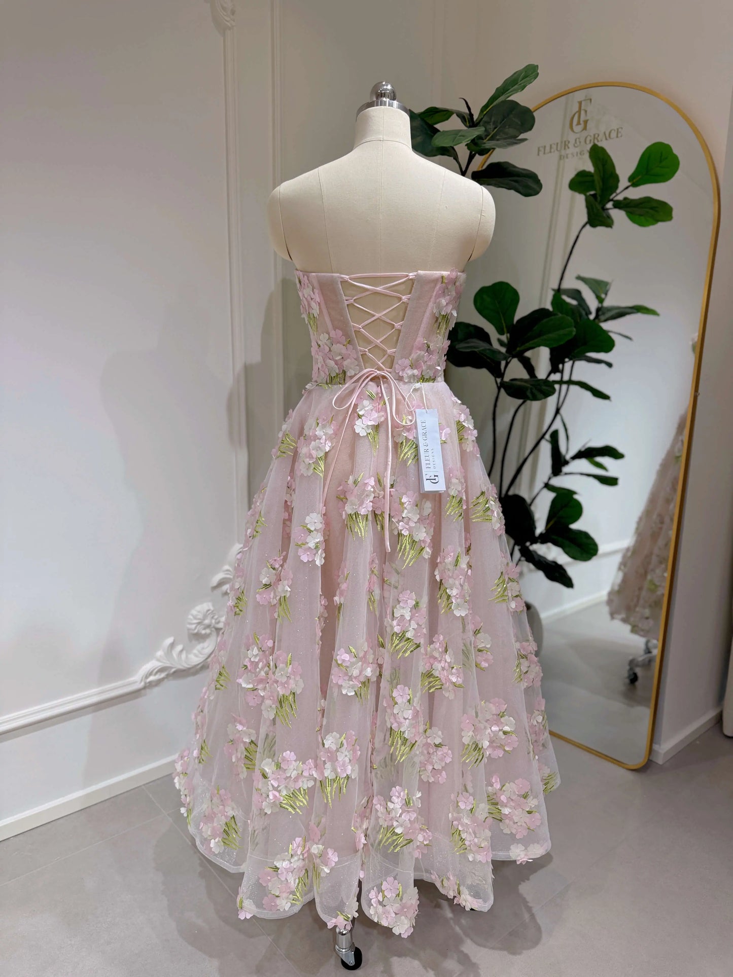 Pink ankle-length gown with 3D hydrangea floral lace, sparkly lining, and a lace-up back on a dress form.