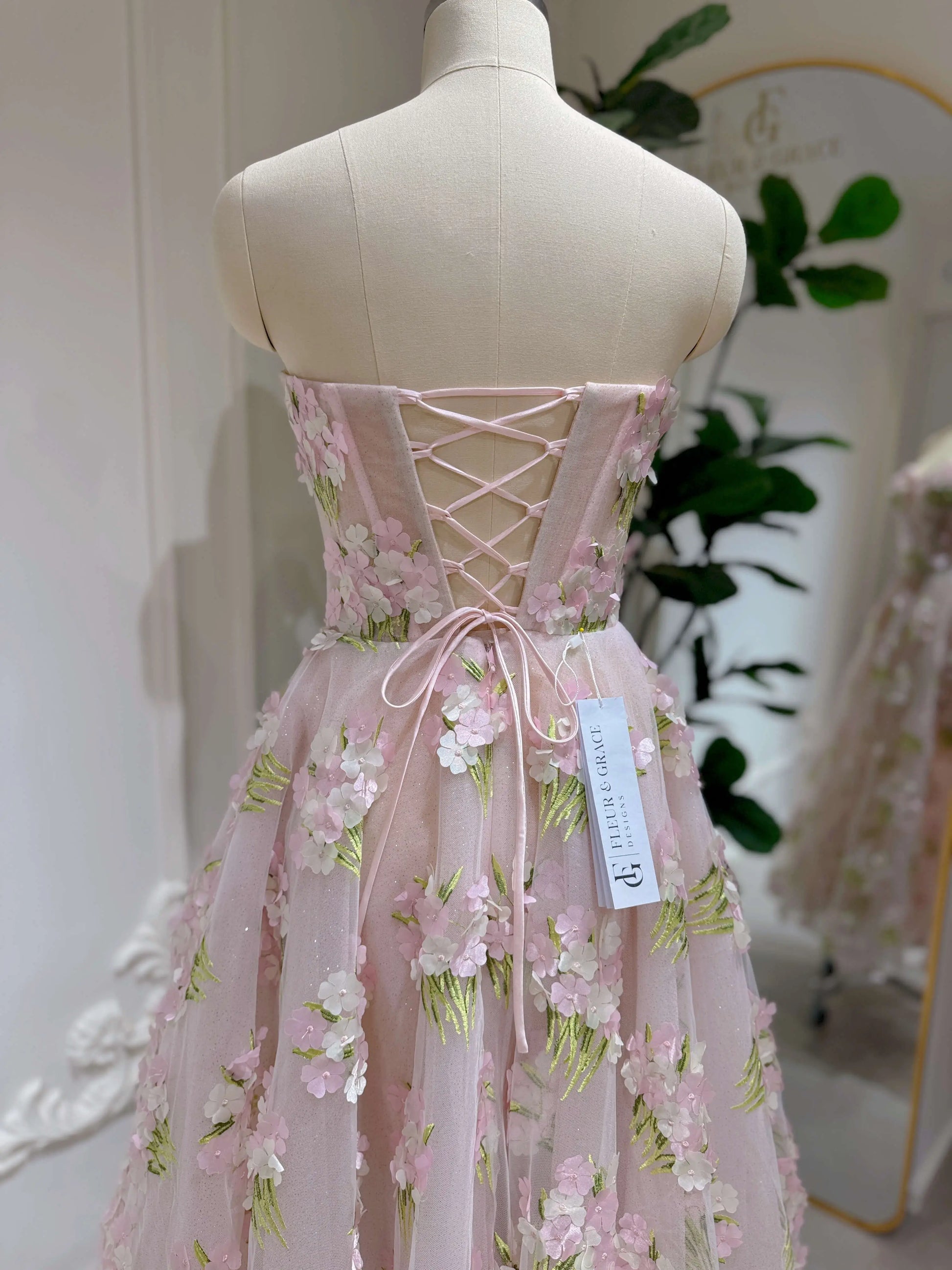 Pink ankle-length gown with 3D hydrangea floral lace, sparkly lining, and a corset-style lace-up back on a mannequin.