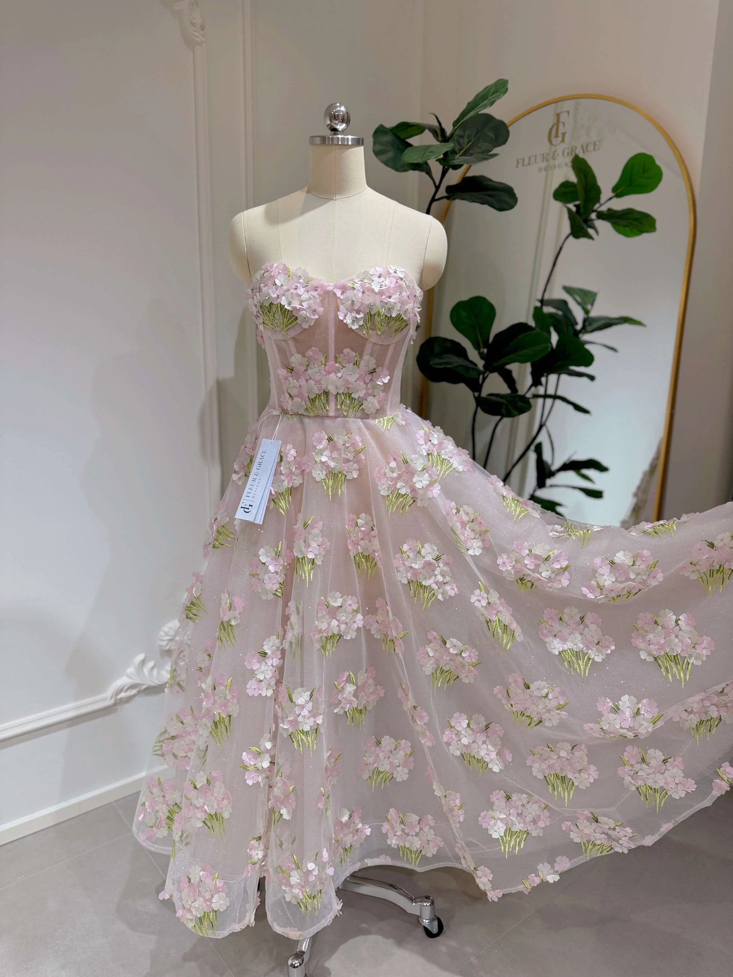 Pink ankle-length gown with 3D hydrangea floral lace, sparkly lining, and a structured bodice on a mannequin.