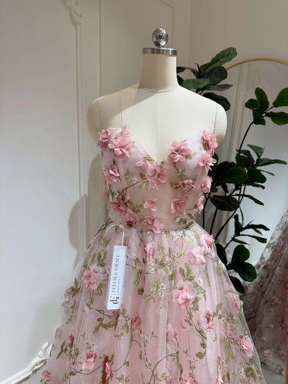 Pink organza prom gown with 3D floral lace, green leaf prints, sweetheart neckline, and sparkly mesh on a mannequin.